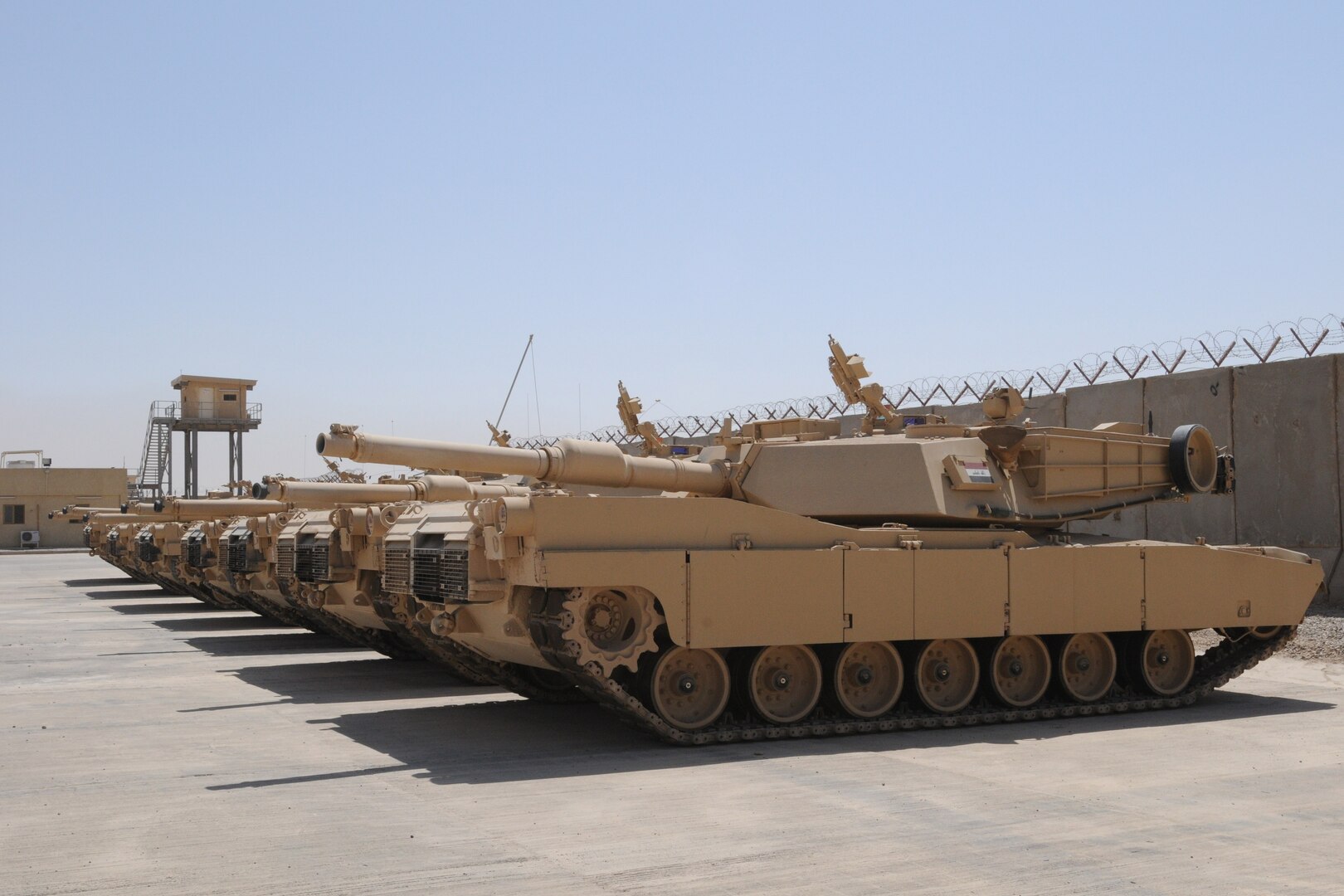 M1A1 tanks lined up on cement inside a desert base