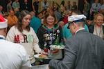 A man with his back to the camera serves food to two women wearing holiday sweaters.