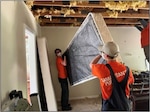 Two people in orange shirts move a bed during hurricane cleanup