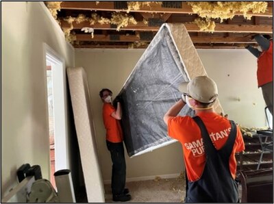 Two people in orange shirts move a bed during hurricane cleanup