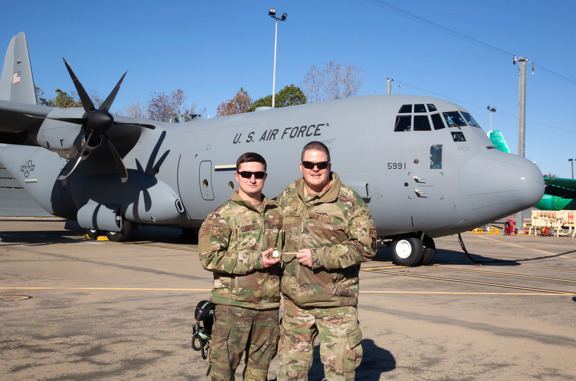 Staff Sgt. Creston Shirey and Master Sgt. Dan Scott, aircraft maintenance craftsmen assigned to the 910th Aircraft Maintenance Squadron, pose for a photo while holding a ceremonial aircraft key in front of the unit’s newest C-130J-30 Super Hercules aircraft at the Lockheed Martin assembly plant in Marietta, Georgia, Dec. 6, 2024.