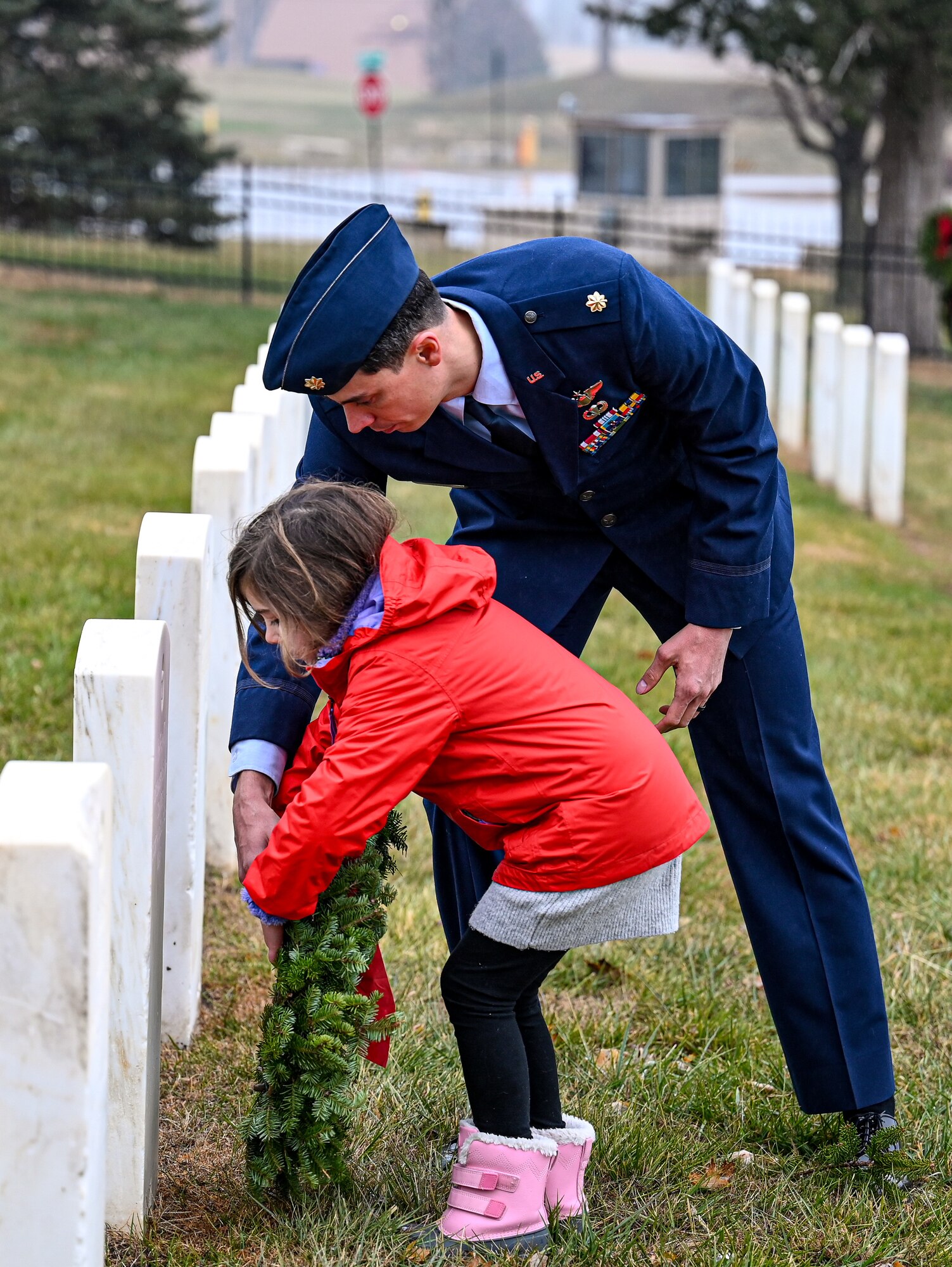 Man helps child lay a wreath on a headstone