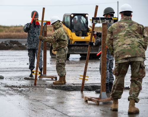 Four U.S. Air Force and Japan Air Self-Defense Force members mark measurements around a crater.