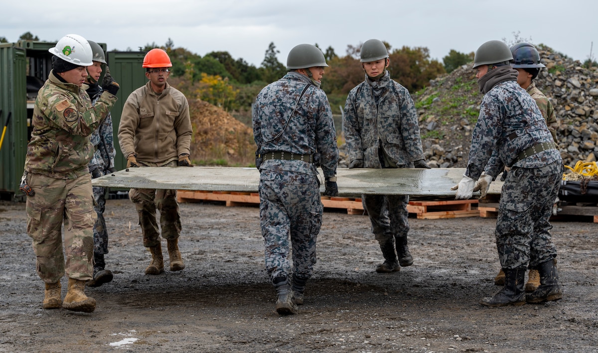 U.S. Air Force and Japan Air Self-Defense Force members carry a flat piece of matting.