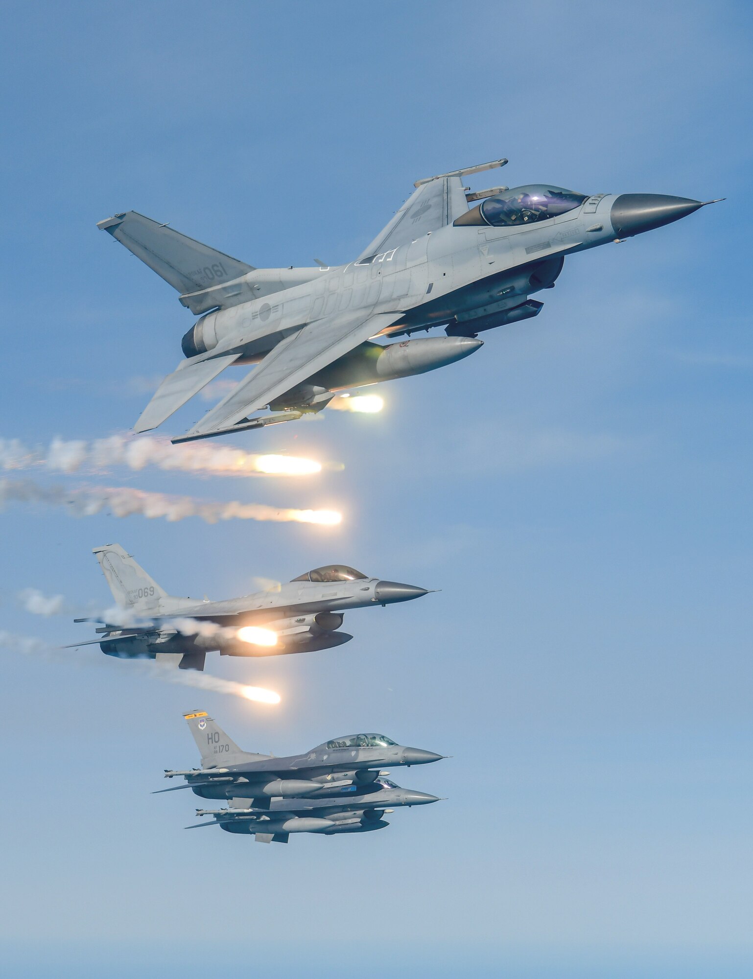 Four F-16s fly in formation with flares being released