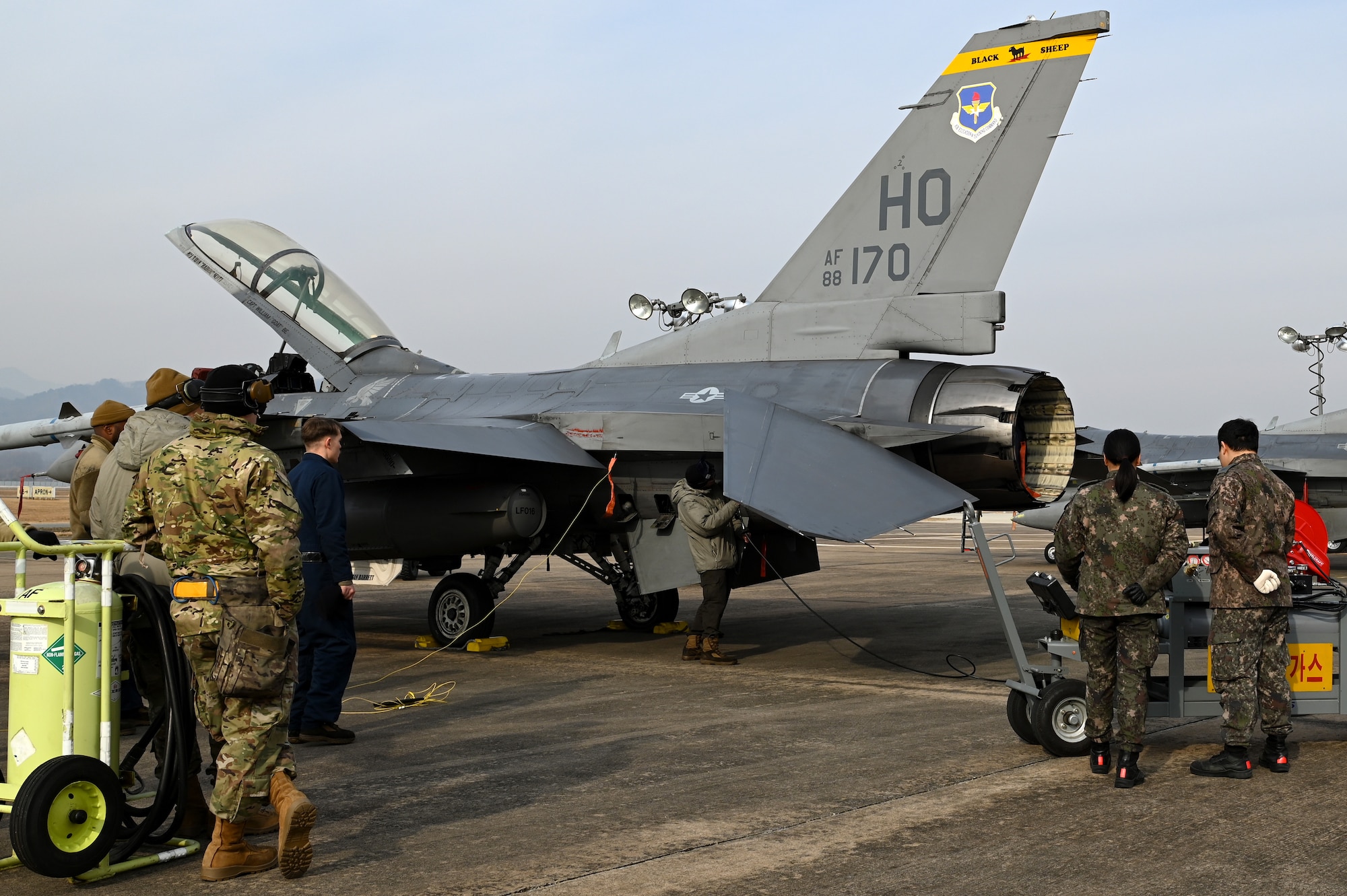 People stand on the flightline by an F-16