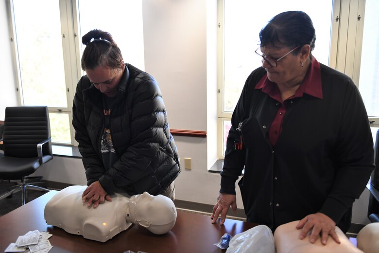 Woman instructs lady on how to perform CPR using a mannequins