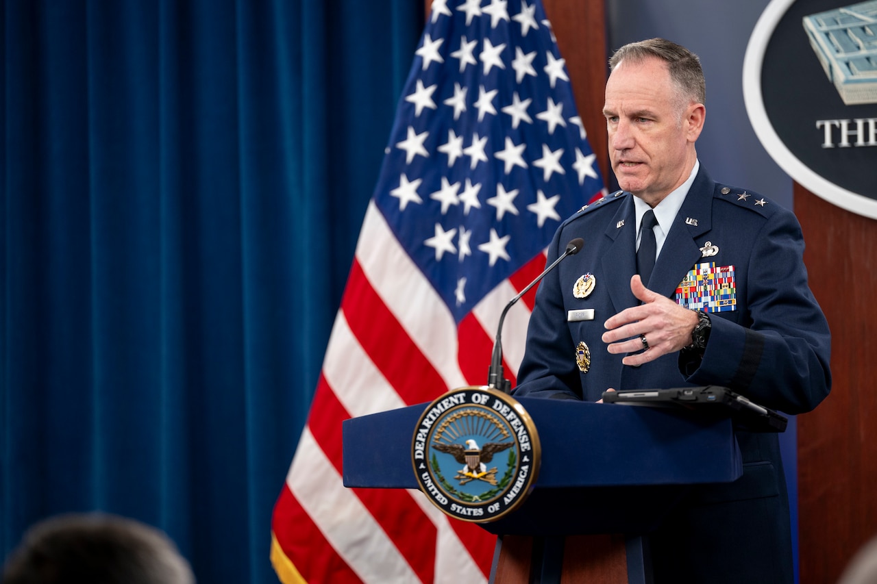 A general speaks from behind a lectern in front of a Pentagon logo and an American flag.