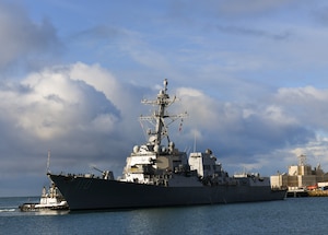 A medium size gray Navy ship leaves port.