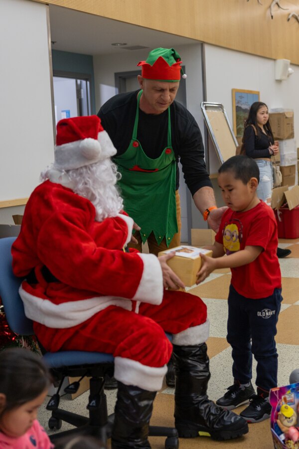 U.S. Marine Corps Pfc. Kasen Lee, dressed as Santa Claus, and Sgt. Maj. Julian Dan, dressed as an elf, hands a toy to a child attending Napaaqtugmiut School in Noatak, Alaska, Dec. 9, 2024. Lee, an administrative specialist with Detachment Delta Company, 4th Law Enforcement Battalion, Force Headquarters Group, and Dan, inspector-instructor command senior enlisted leader, Force Headquarters Group, delivered toys to the school with the assistance of Marines from Detachment Delta Company and U.S. Airmen from various units during this year’s Toys for Tots operation. The Toys for Tots mission exemplifies the Marine Corps spirit in the Last Frontier, strengthening community ties while sharpening the Marines' readiness for Arctic operations. (U.S. Marine Corps photo by Sgt. Ethan M. LeBlanc)
