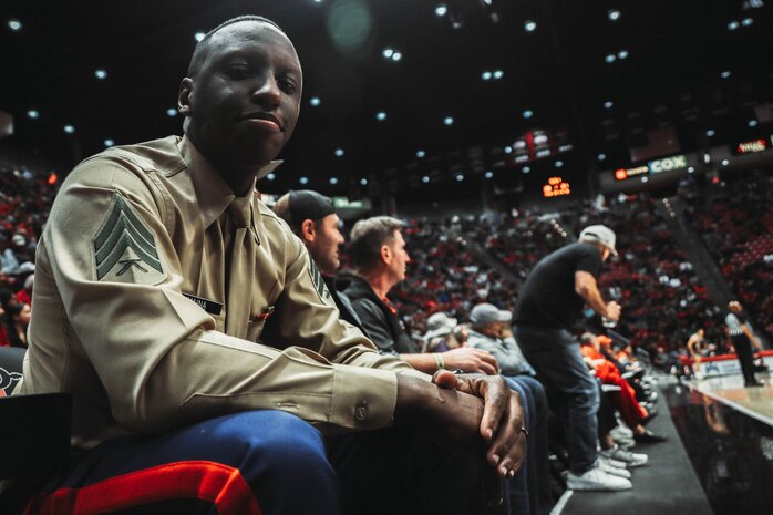 U.S. Marine Corps Sgt. Dennis Maina, assistant for Officer Selection Team San Diego, Recruiting Station San Diego, poses for a photograph during a San Diego State University Men's Basketball game in San Diego, California, Dec. 11, 2024. Maina was recognized as the guest of honor during the game. The guest of honor received special recognition including a formal introduction, reserved seating and participation in game-day activities. (U.S. Marine Corps photo by Cpl. Alejandro Fernandez)