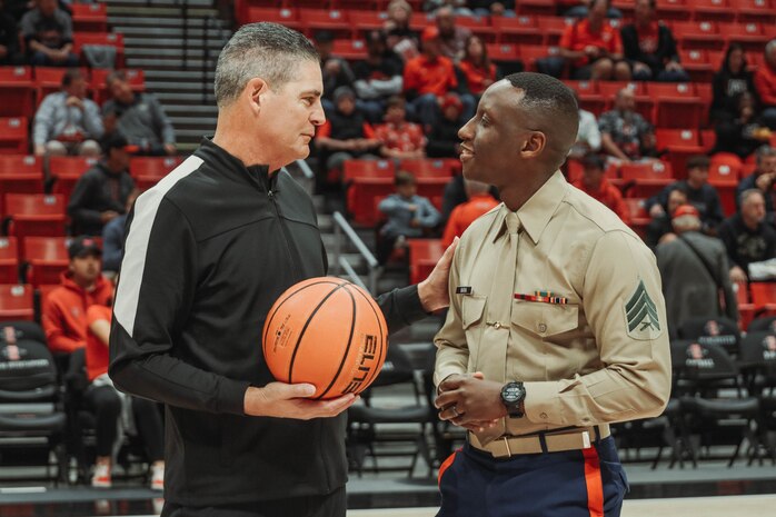 U.S. Marine Corps Sgt. Dennis Maina, assistant for Officer Selection Team San Diego, Recruiting Station San Diego,  talks to a referee during the San Diego State University Men's Basketball game in San Diego, California, Dec. 11, 2024. Maina was recognized as the guest of honor during the game. The guest of honor received special recognition including a formal introduction, reserved seating and participation in game-day activities. (U.S. Marine Corps photo by Cpl. Alejandro Fernandez)