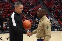 U.S. Marine Corps Sgt. Dennis Maina, assistant for Officer Selection Team San Diego, Recruiting Station San Diego,  presents the game ball to the referee during the San Diego State University Men's Basketball game in San Diego, California, Dec. 11, 2024. Maina was recognized as the guest of honor during the game. The guest of honor received special recognition including a formal introduction, reserved seating and participation in game-day activities. (U.S. Marine Corps photo by Cpl. Alejandro Fernandez)