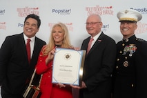 Hollywood Christmas Parade hosts Dean Cain and Laura McKenzie present a Los Angeles County Sheriffs certificate for the Toys for Tots Foundation to retired U.S. Marine Corps Lt. Gen. James Laster, president and CEO of the Toys for Tots Foundation, and U.S. Marine Corps Lt. Gen. Leonard Anderson, commander of U.S. Marine Corps Forces Reserve and U.S. Marine Corps Forces South, during the 92nd Hollywood Christmas Parade in Hollywood, California, Dec. 1, 2024. The mission of the Toys for Tots Holiday Program is to collect new, unwrapped toys, books, and other gifts and distribute them to less fortunate children at Christmastime. The Hollywood Christmas Parade is an annual American parade held on the Sunday after Thanksgiving in Hollywood; it follows a 3.5-mile route along Hollywood Boulevard, then back along Sunset Boulevard, featuring various celebrities. (U.S. Marine Corps photo by Cpl. Fred Garcia)