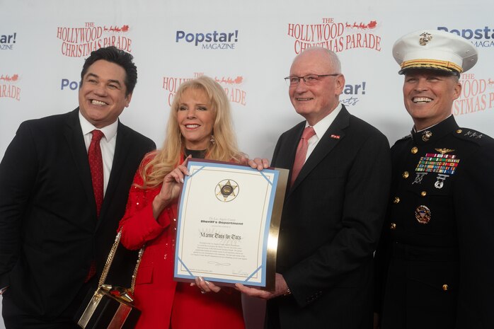 Hollywood Christmas Parade hosts Dean Cain and Laura McKenzie present a Los Angeles County Sheriffs certificate for the Toys for Tots Foundation to retired U.S. Marine Corps Lt. Gen. James Laster, president and CEO of the Toys for Tots Foundation, and U.S. Marine Corps Lt. Gen. Leonard Anderson, commander of U.S. Marine Corps Forces Reserve and U.S. Marine Corps Forces South, during the 92nd Hollywood Christmas Parade in Hollywood, California, Dec. 1, 2024. The mission of the Toys for Tots Holiday Program is to collect new, unwrapped toys, books, and other gifts and distribute them to less fortunate children at Christmastime. The Hollywood Christmas Parade is an annual American parade held on the Sunday after Thanksgiving in Hollywood; it follows a 3.5-mile route along Hollywood Boulevard, then back along Sunset Boulevard, featuring various celebrities. (U.S. Marine Corps photo by Cpl. Fred Garcia)