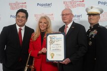Hollywood Christmas Parade hosts Dean Cain and Laura McKenzie present a Los Angeles certificate of recognition for the Toys for Tots Foundation to retired U.S. Marine Corps Lt. Gen. James Laster, president and CEO of the Toys for Tots Foundation, and U.S. Marine Corps Lt. Gen. Leonard Anderson, commander of U.S. Marine Corps Forces Reserve and U.S. Marine Corps Forces South, during the 92nd Hollywood Christmas Parade in Hollywood, California, Dec. 1, 2024. The mission of the Toys for Tots Holiday Program is to collect new, unwrapped toys, books, and other gifts and distribute them to less fortunate children at Christmastime. The Hollywood Christmas Parade is an annual American parade held on the Sunday after Thanksgiving in Hollywood; it follows a 3.5-mile route along Hollywood Boulevard, then back along Sunset Boulevard, featuring various celebrities. (U.S. Marine Corps photo by Cpl. Fred Garcia)
