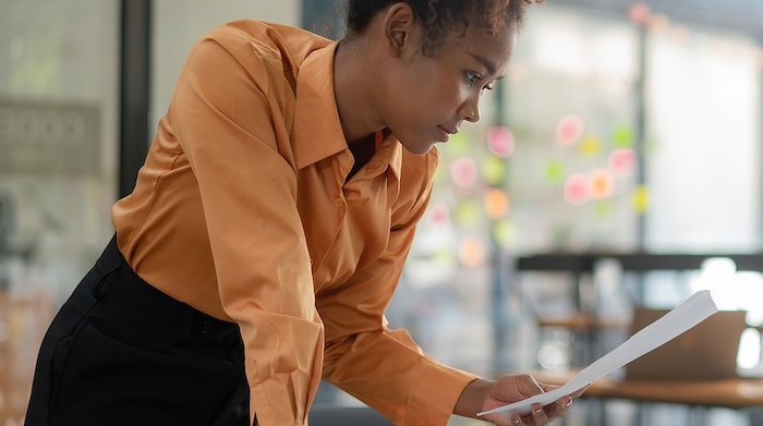 A young black woman wearing an orange blouse and skirt looking at her desk at her NSA application