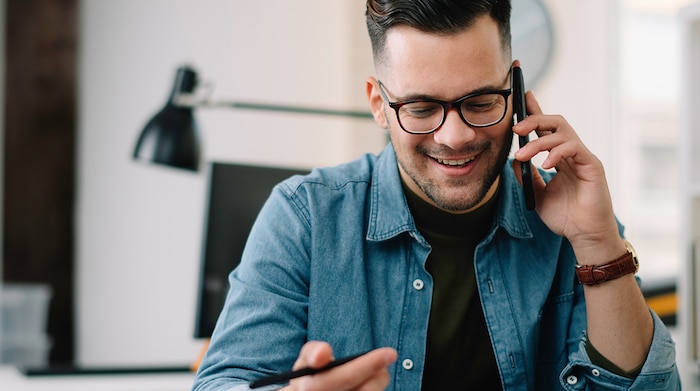 A white male wearing glasses is sitting at a desk talking on a cell phone to an NSA recruiter