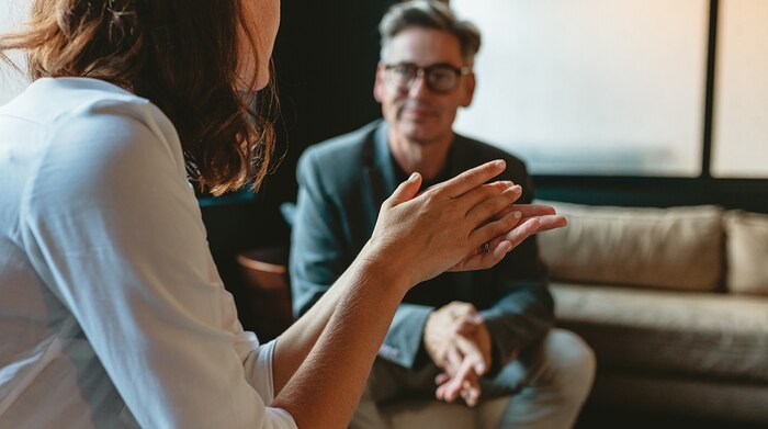 A woman having a conversation with a middle-aged white man who is sitting on a couch during an NSA interview