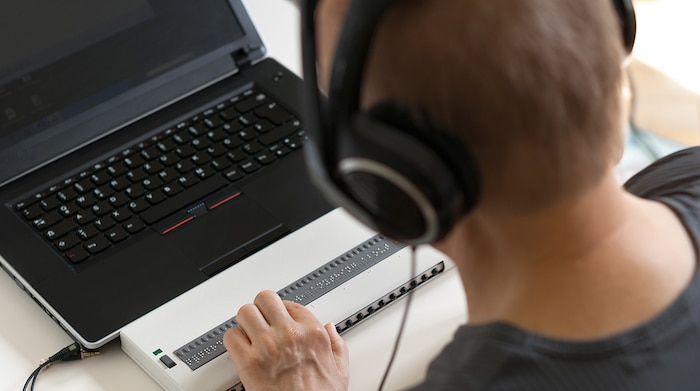 A man sitting at a computer, using a braille reader to understand what is on the screen while completing an application