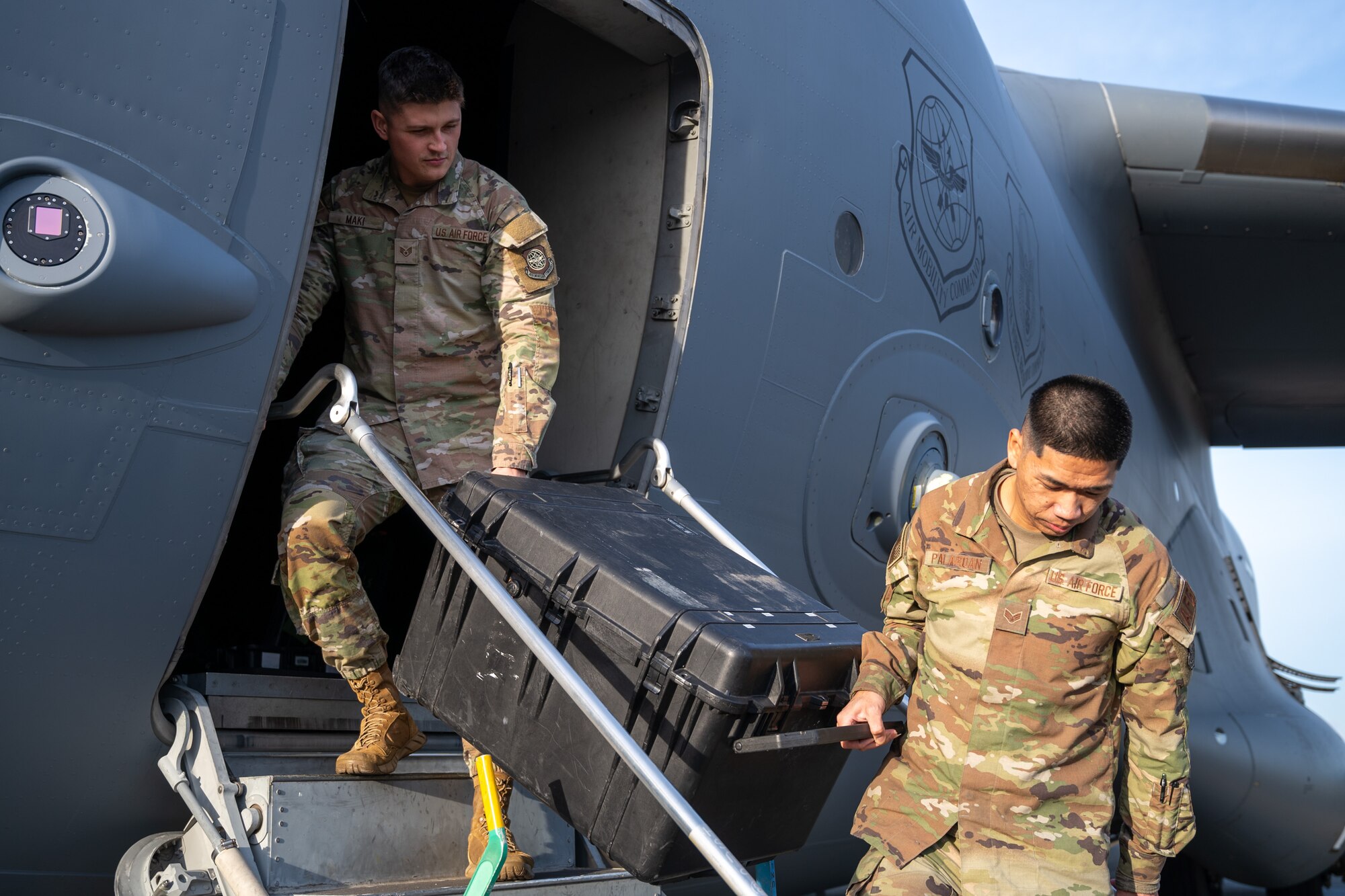 U.S. Air Force Staff Sgt. Spencer Maki, left, and Senior Airman Brysen Palaroan, both 62d Operations Support Squadron aircrew flight equipment technicians, unload an AFE case from a C-17 Globemaster III at Joint Base Lewis-McChord, Washington, Dec. 10, 2024.