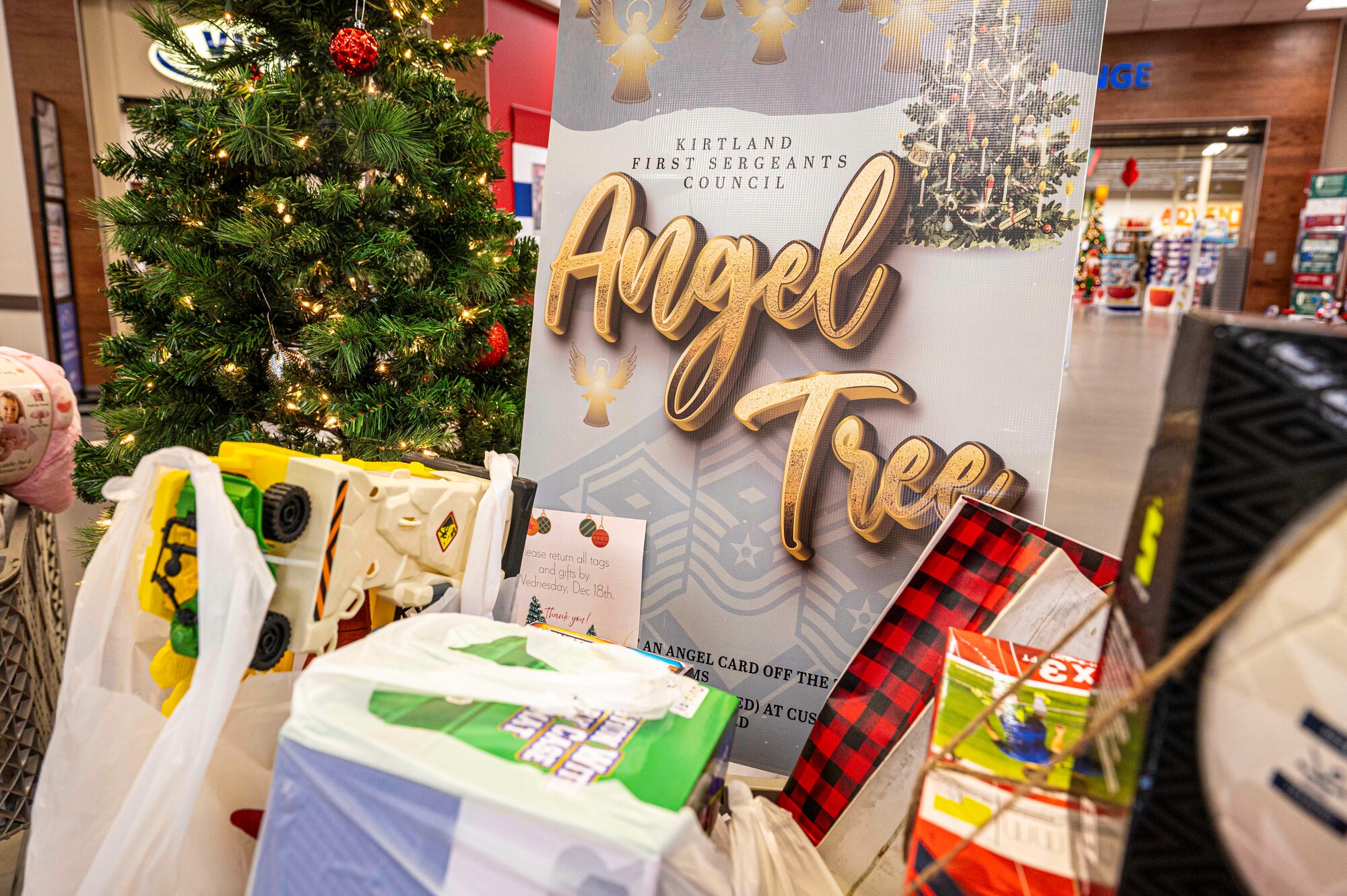 Close up photo of angel tree sign, christmas tree, and gifts in the foreground
