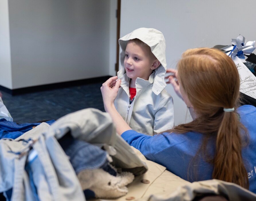 A small child wears a new jacket and his mother adjusts the hood.
