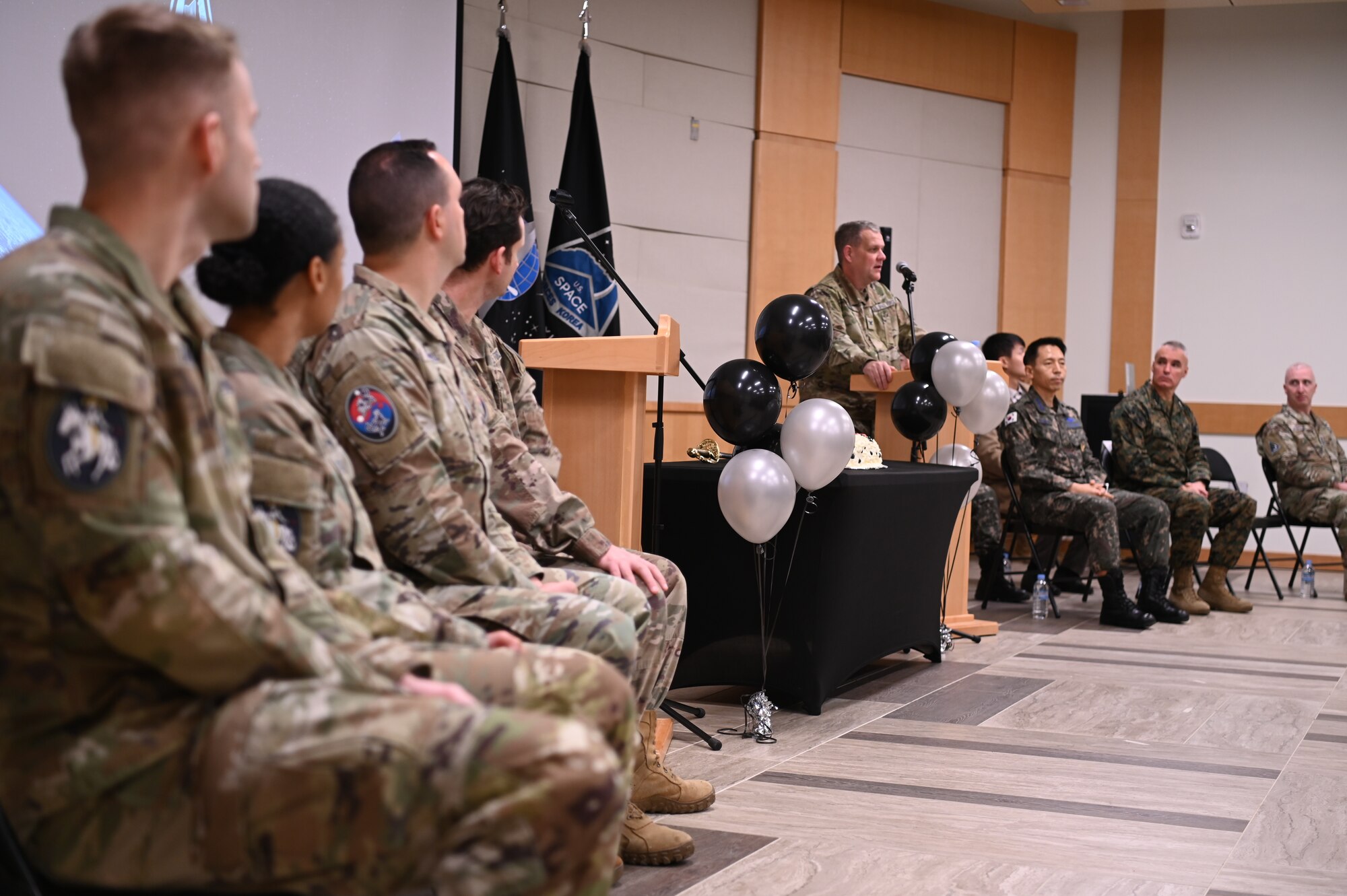 A man in military uniform stands at a podium, U.S. and Republic of Korea servicemembers watch from chairs on both sides as he addresses the audience.