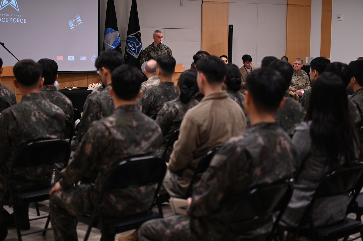 A Marine stands at a podium in front of an audience of U.S. and Republic of Korea Air Force members.