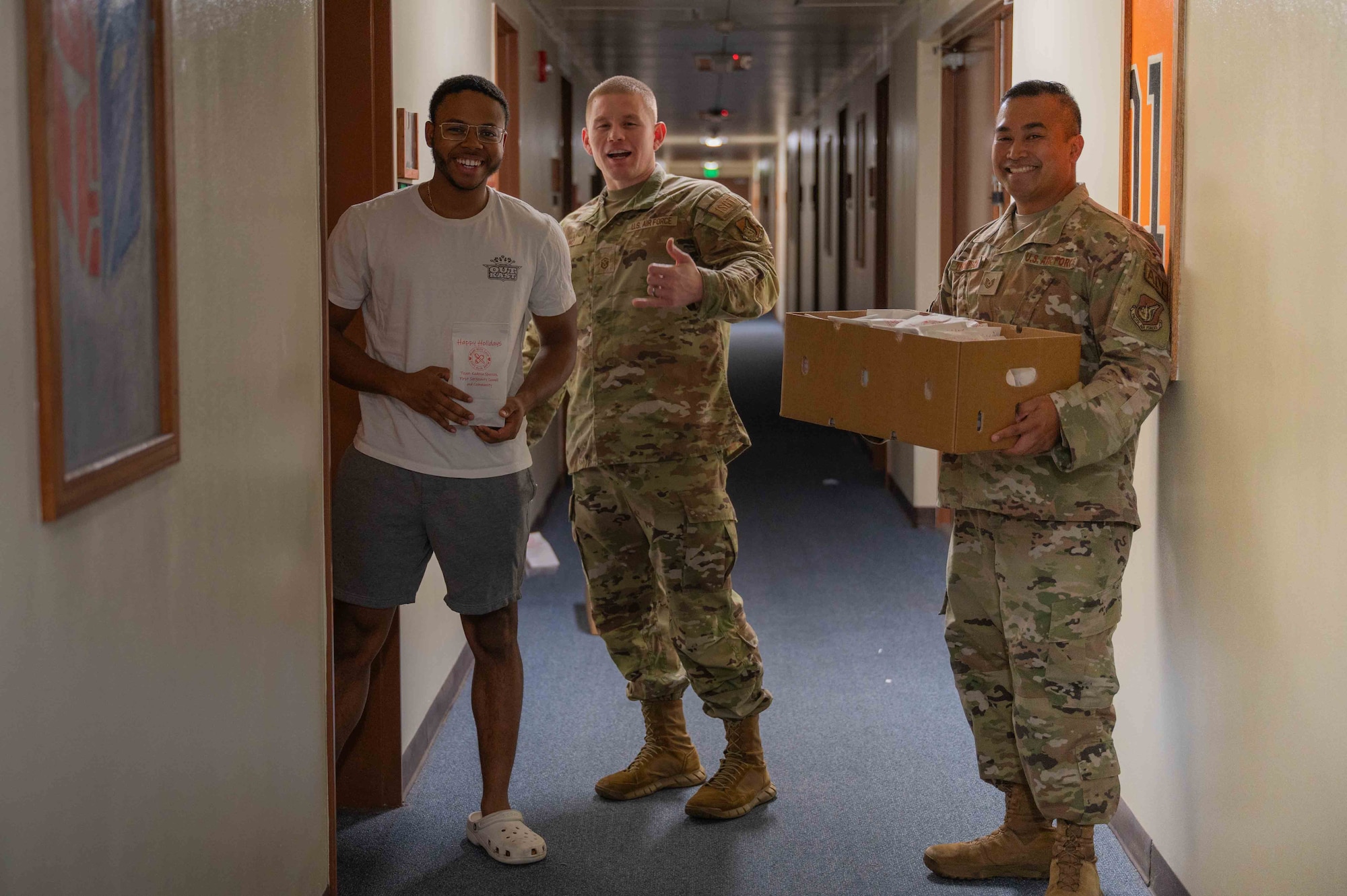 military members hand a bag of cookies to a dorm resident in the hall in front of residents room
