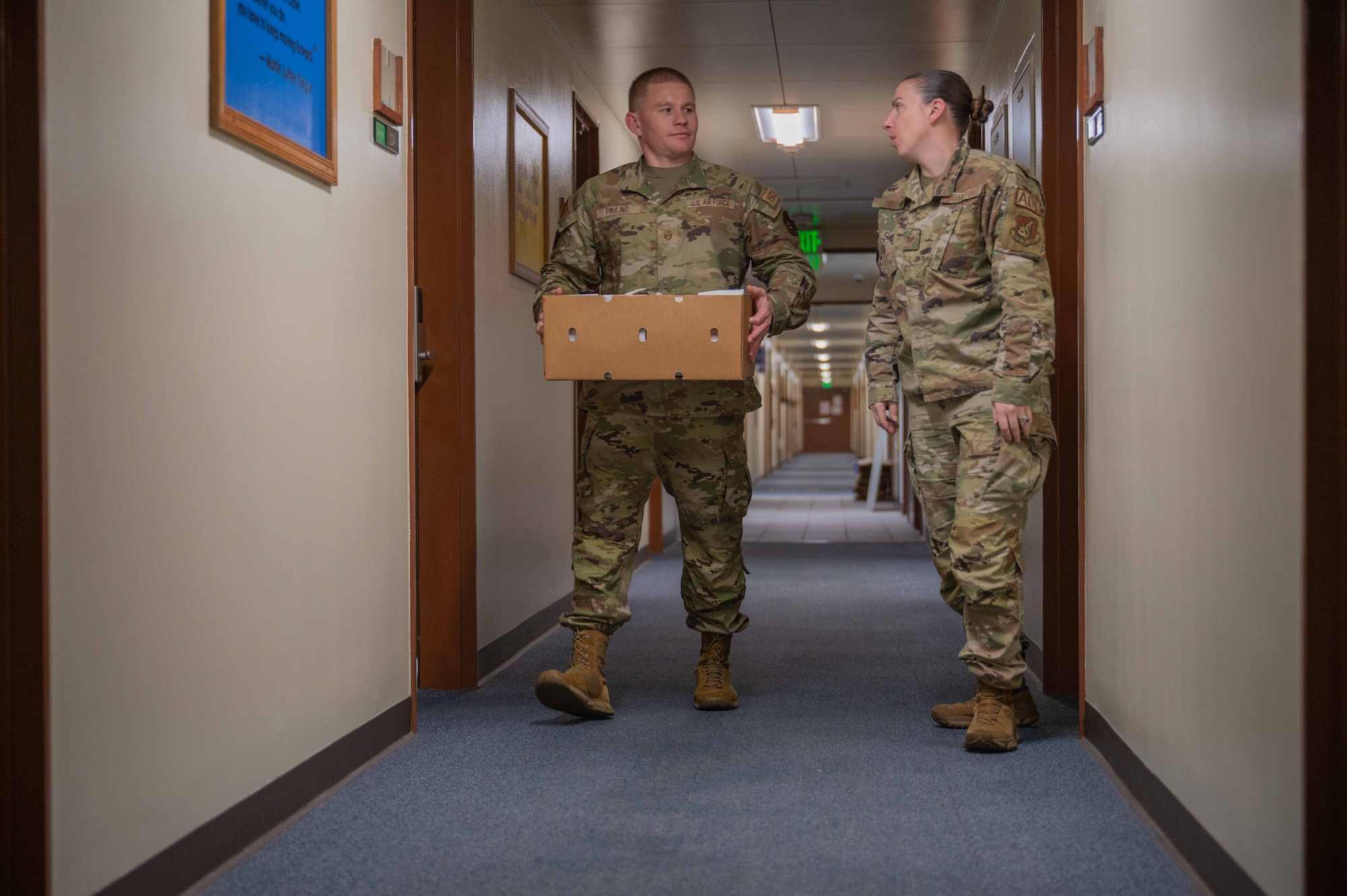 two military members walk down the hall while holding a box full of cookie bags