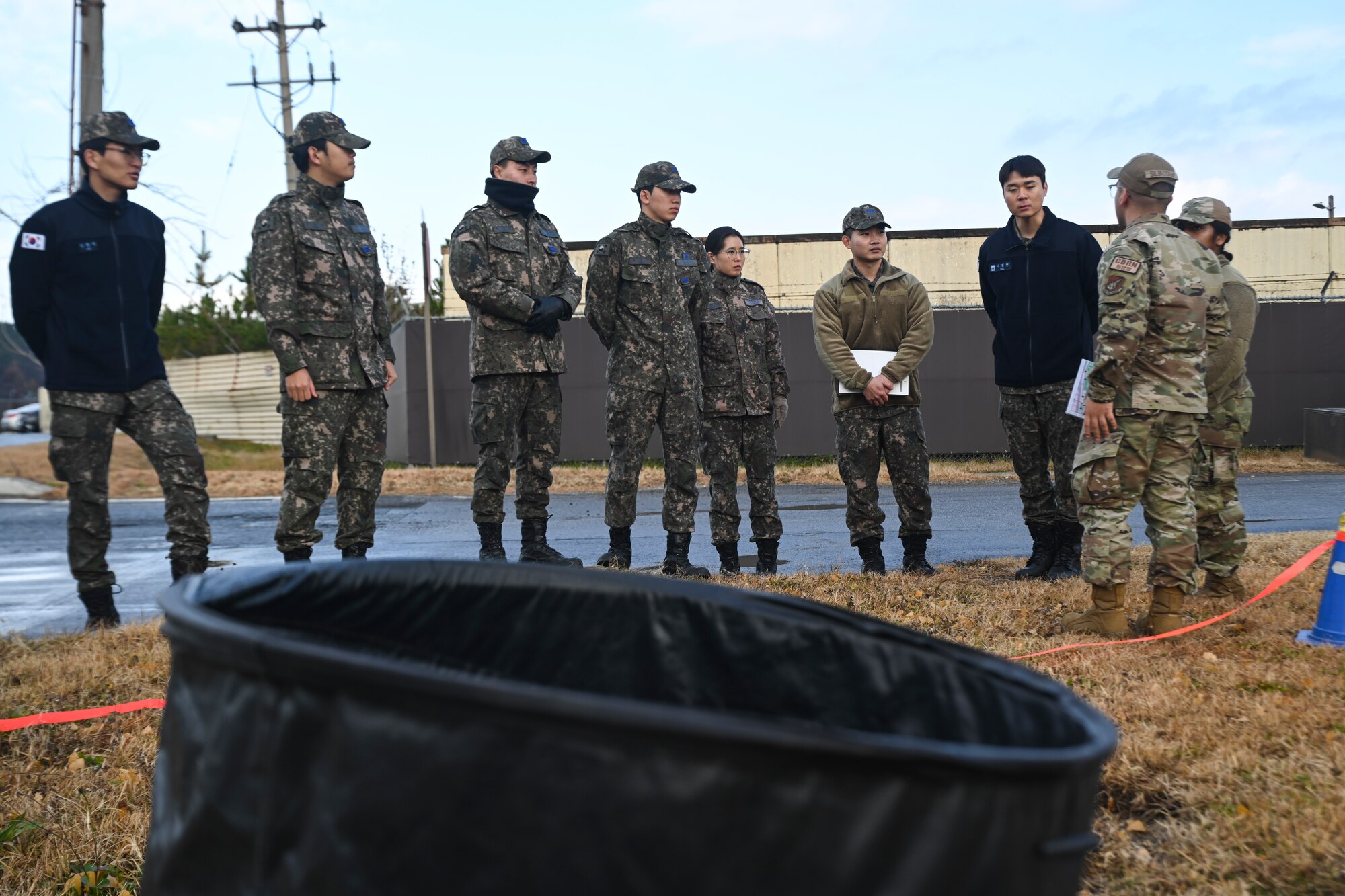 U.S. and Republic of Korea Air Force Airmen discuss Chemical, Biological, Radiological, and Nuclear training tactics and procedures near a simulated contaminated waste disposal area at Kunsan Air Base