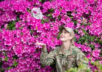 woman in uniform tosses crown in the air in front of purple flowers