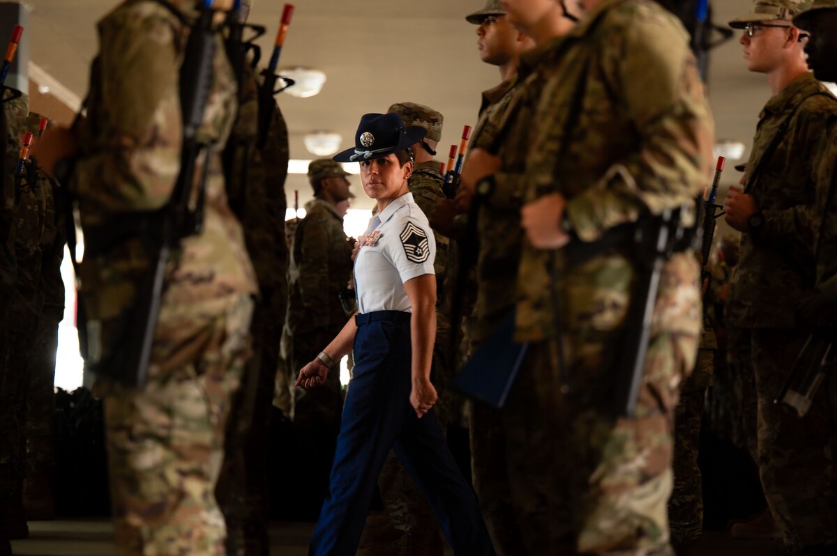 woman in uniform marches through a crowd of trainees and stares directly into the camera