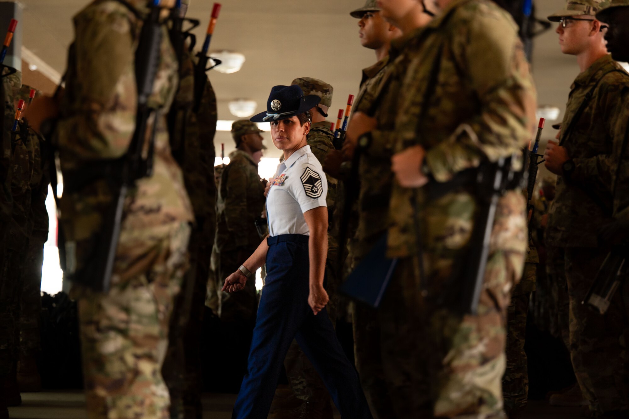 woman in uniform marches through a crowd of trainees and stares directly into the camera