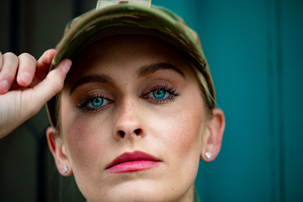 woman in uniform stares directly into camera with bright blue eyes and pink lipstick