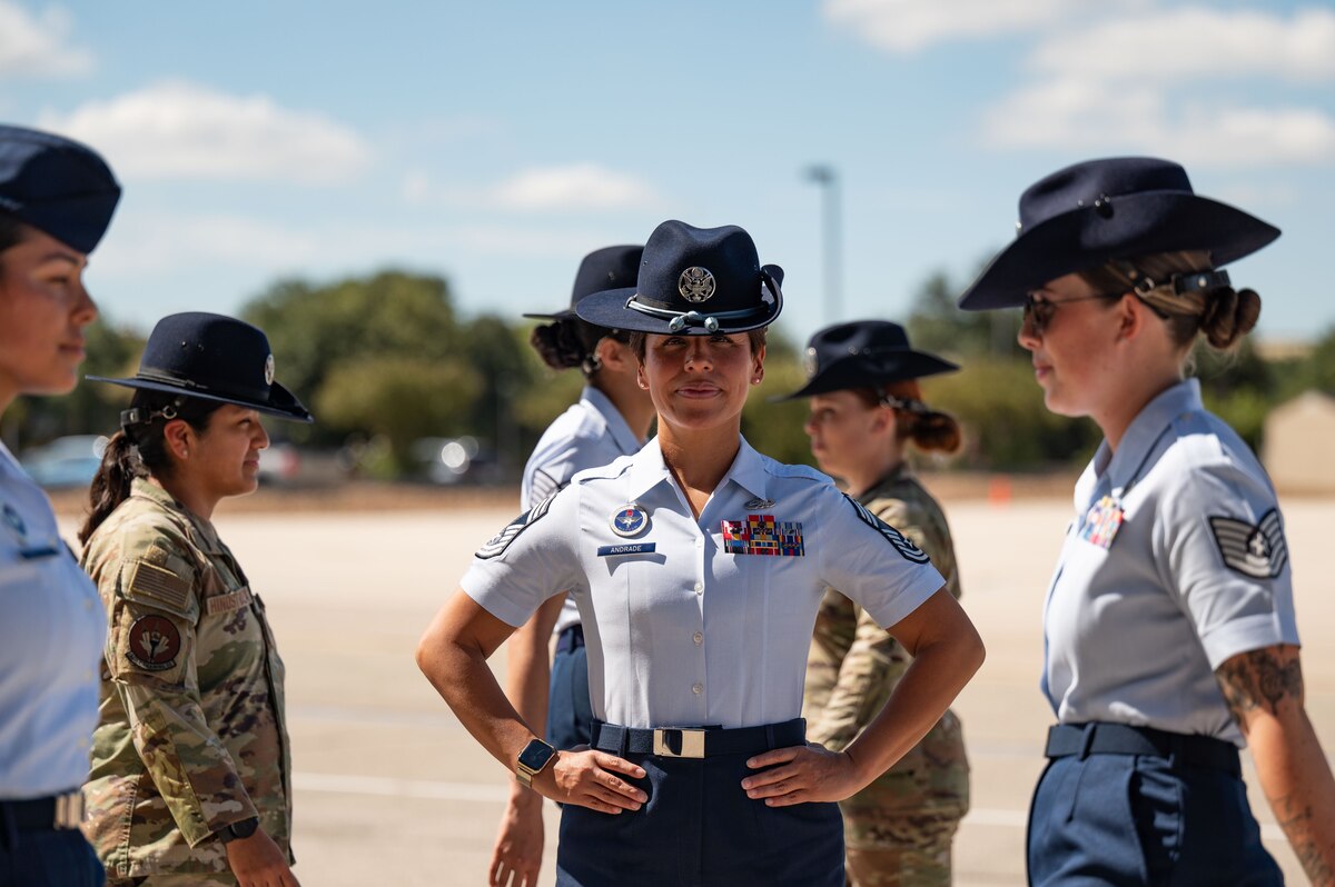 women in uniform walk in front of the camera; one woman stares straight into the lens