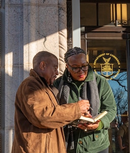 Two civilians looking at a notebook and jotting down notes together