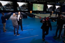 A civilian is interviewed by media on stage while standing