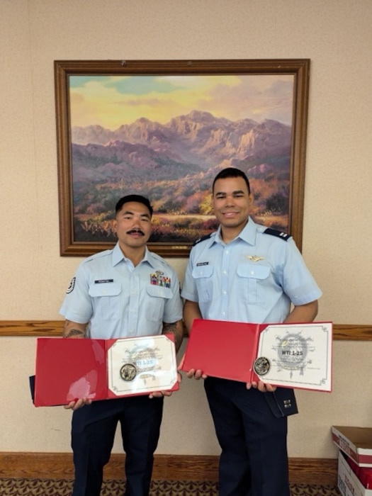 Two Airmen holding certificates after graduating a course