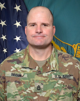 Man in U.S. Army uniform standing in front of two flags.