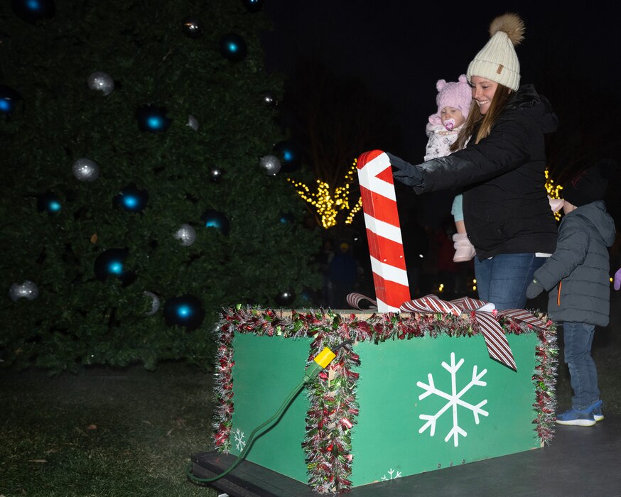 A woman holding a toddler pushes a large, ornate switch.
