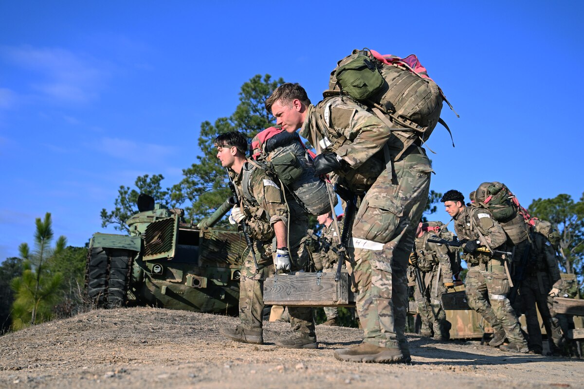 Soldiers carrying ruck sacks carry large, weighted ammo crates as part of a training exercise.