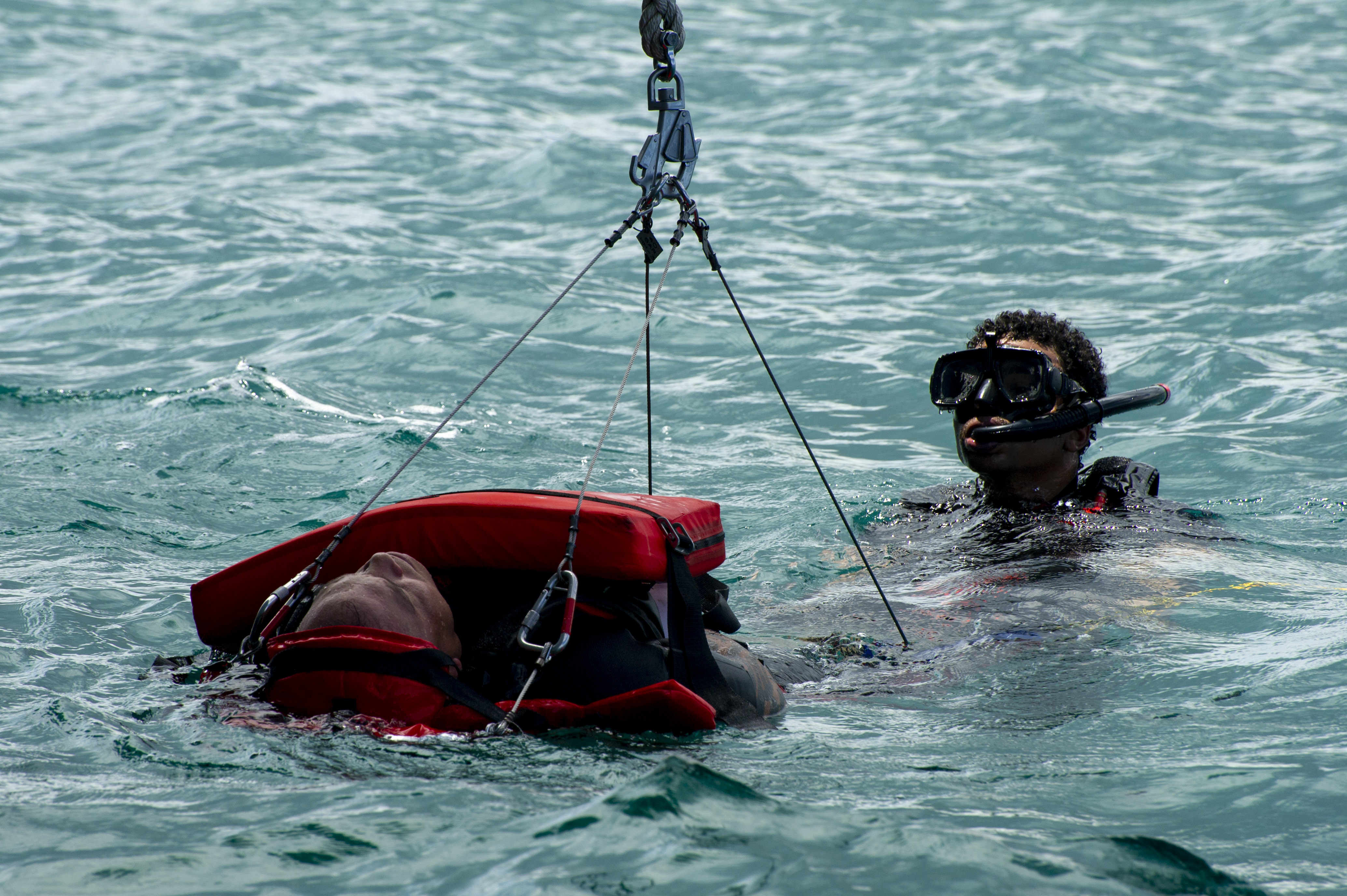 From left, Military Sealift Command civil service mariners Eric Nanpei and Christopher Baker, search and rescue (SAR) swimmers assigned to the Emory S. Land-class submarine tender USS Frank Cable (AS 40) practice using a MedEvac litter during a SAR exercise conducted in Apra Harbor, July. 31. Frank Cable, forward-deployed to the island of Guam, repairs, rearms, and re-provisions submarines and surface vessels in the Indo-Pacific region.