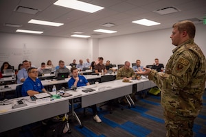 Photo shows man speaking to classroom of people