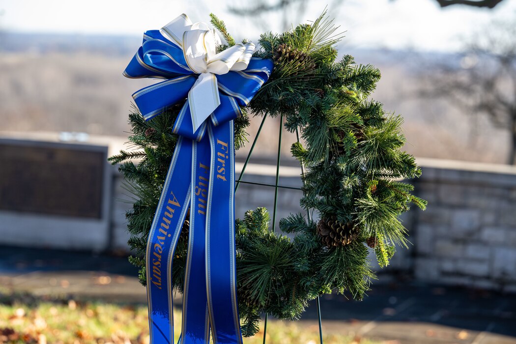 A wreath with a blue bow stating "First Flight Anniversary" is pictured outside