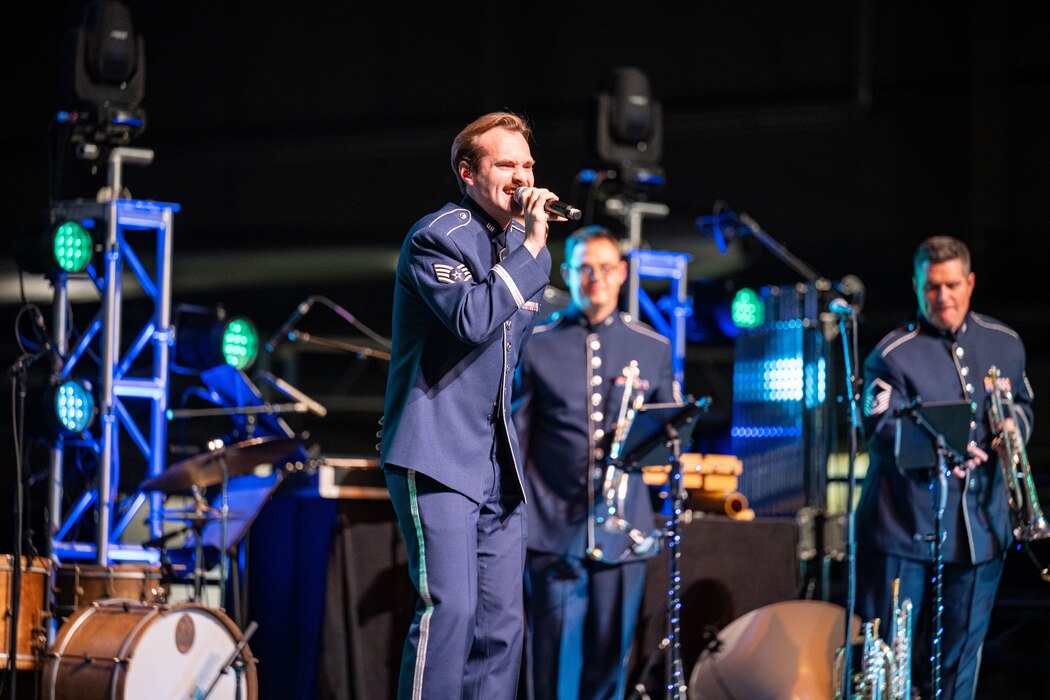 A man wearing a service dress uniform sings on stage during a holiday concert.