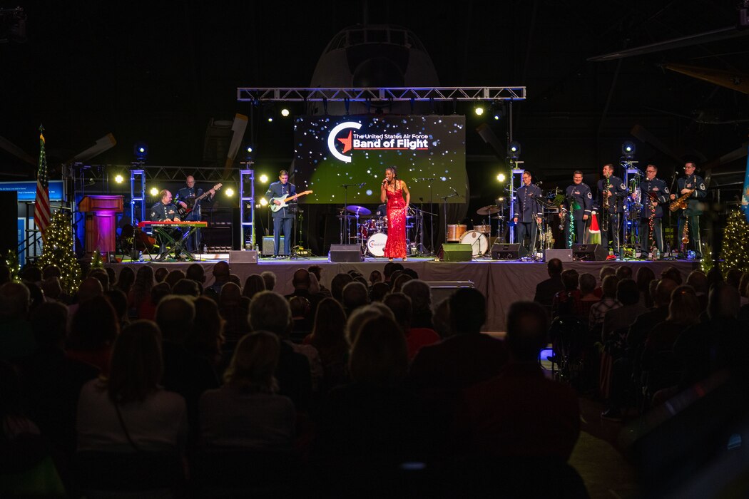 A women in a red dress signs while other band members perform on stage during a concert.