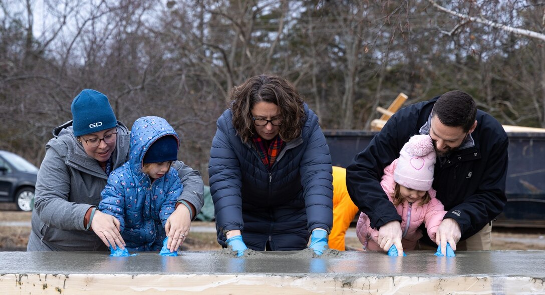 Annie Colaluca, Executive Director of Early Learning and Family Services for the Bath Area Family YMCA, joins two children of BIW shipbuilders as they press handprints into a cement slab that will be used for the new childcare center’s bicycle rack.