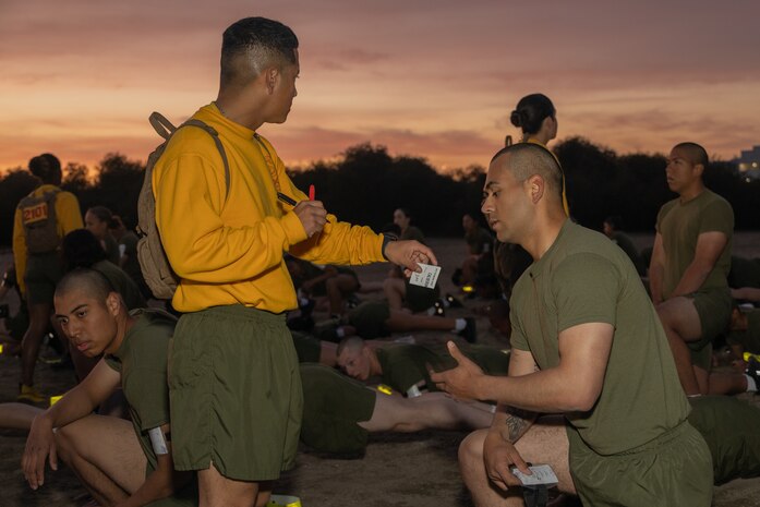 U.S. Marine Corps Drill Instructor, Sgt. Felipe Morales, left, hands a scorecard to Rct. Francisco Calderon, both with Echo Company, 2nd Recruit Training Battalion, during the plank portion of a physical fitness test at Marine Corps Recruit Depot San Diego, California, Dec. 16, 2024. The PFT is an evaluation that all recruits must pass and sets the standards all Marines must maintain once a year to assess battle readiness as well as physical conditioning. The Marine Corps is a professional, disciplined, and capable force. Honor, courage, and commitment are seen and felt in the shared experiences, hardships and challenges we face together in training, and in combat. These values embody what it is to be a Marine, and they live in the collective soul of our Corps. (U.S. Marine Corps photo by Lance Cpl. Janell B. Alvarez)